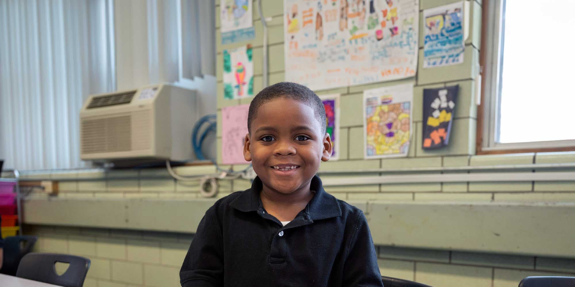 Smiling young student in a classroom decorated with student artwork.