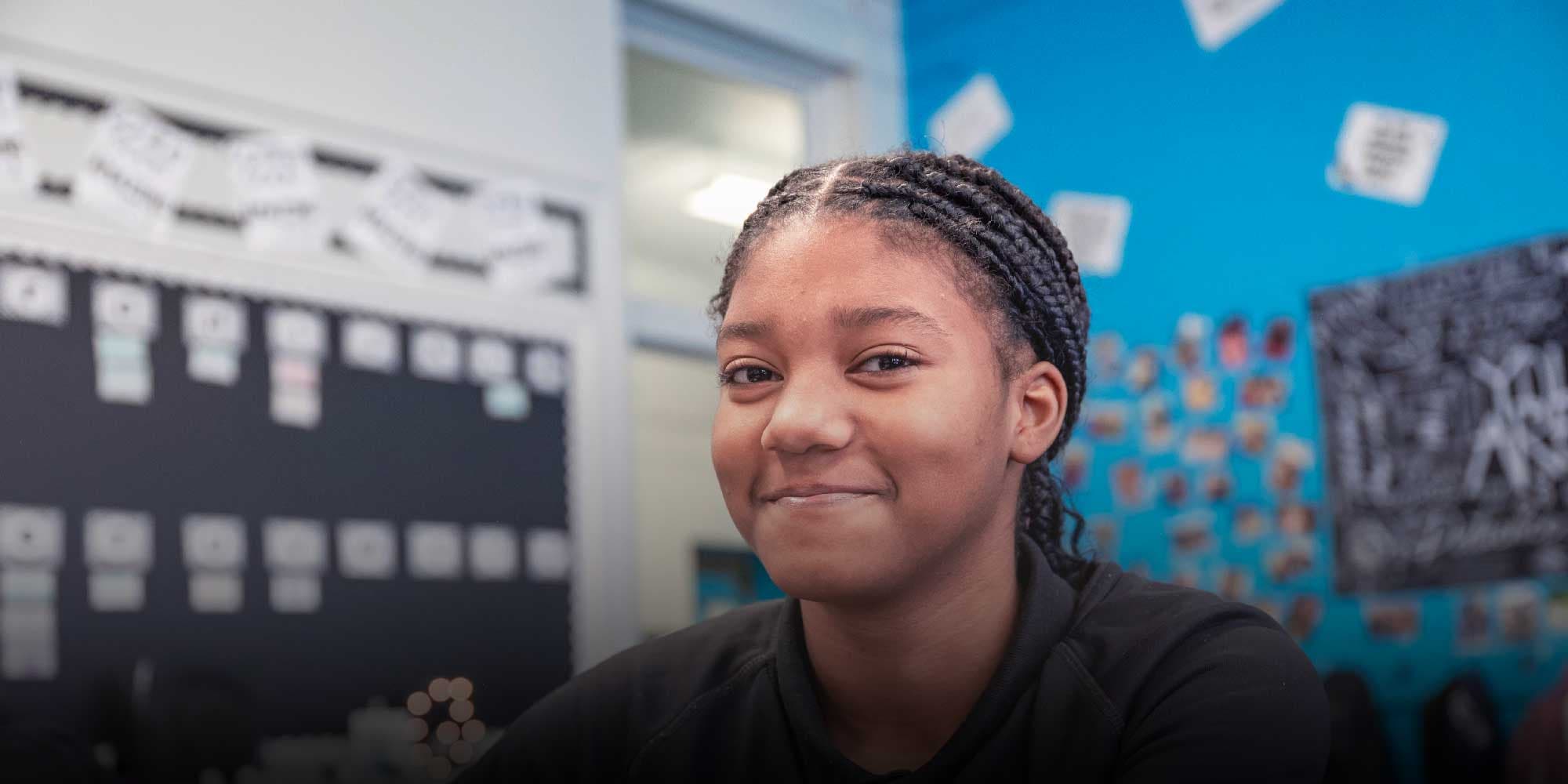 Smiling student with braided hair in a classroom.